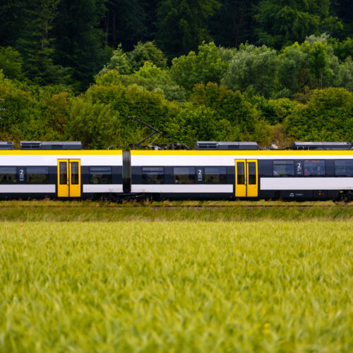 Train passing in Neckar valley near Tübingen Germany on a summer day. Railroad to Stuttgart amidst green wheat fields and forests. Landscape panorama with white and yellow multiple unit